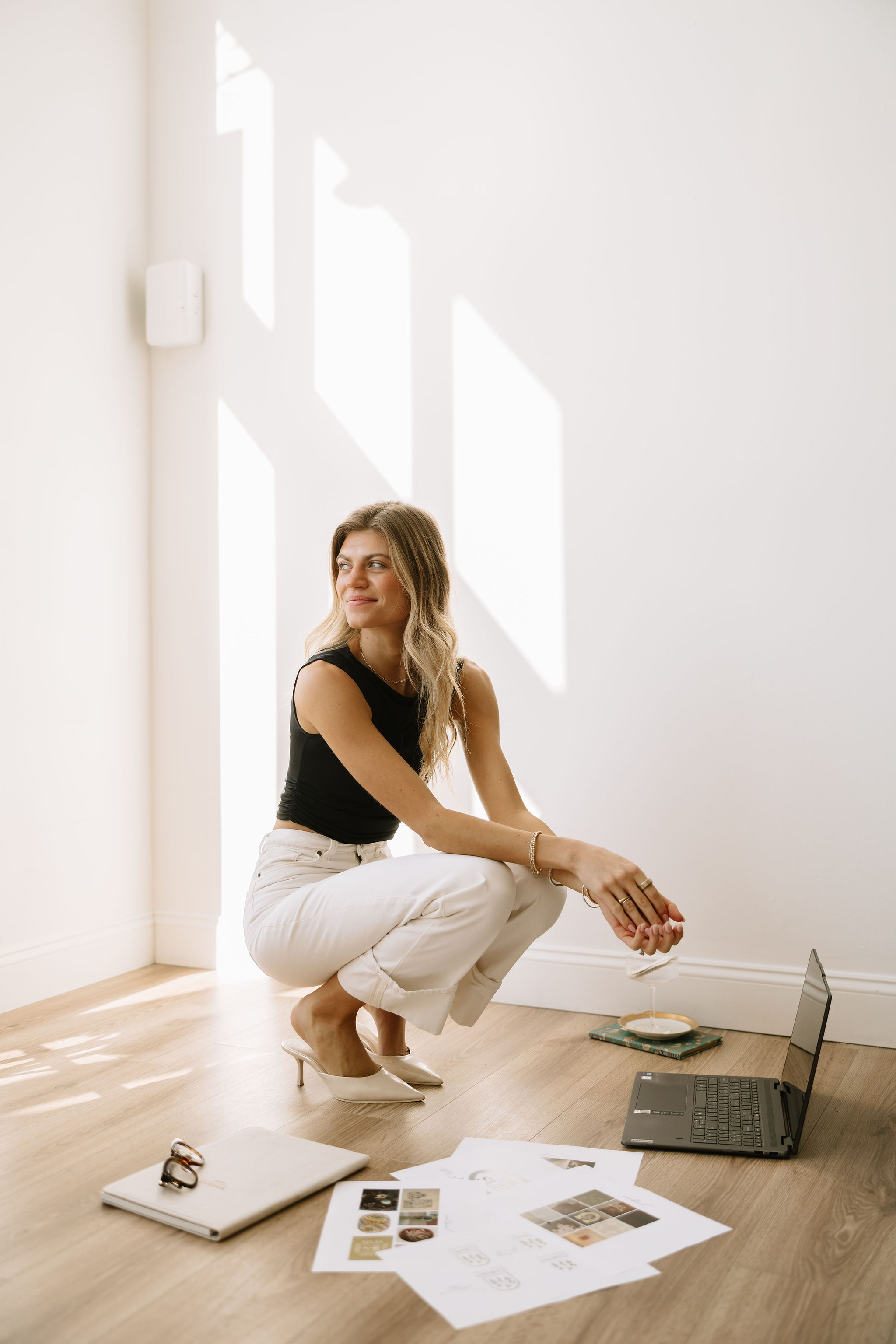 Founder crouching with branding mood boards, laptop, and creative materials in a bright white studio.
