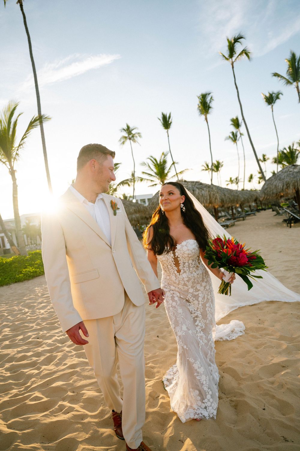 Bride and groom walking hand in hand on a palm-lined beach at sunset
