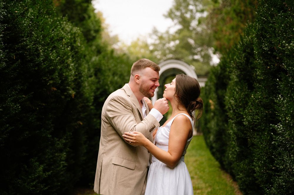 Couple laughing together in a garden path lined with tall hedges