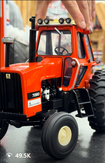 Hands adjusting an orange Allis-Chalmers 7060 toy tractor during an unboxing reel