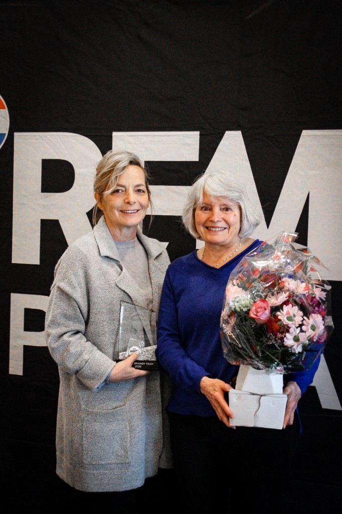 RE/MAX Pinnacle team members with a Brandt Team award and congratulatory flowers