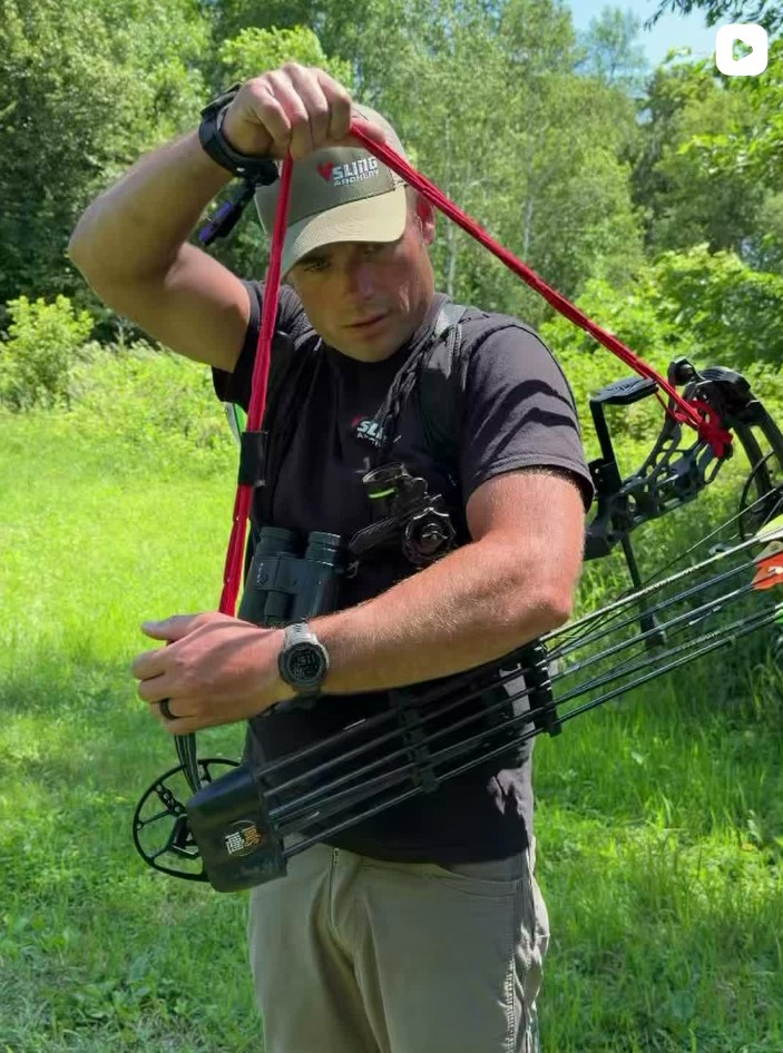 Hunter demonstrating a red Vsling bow sling over the shoulder in a grassy field