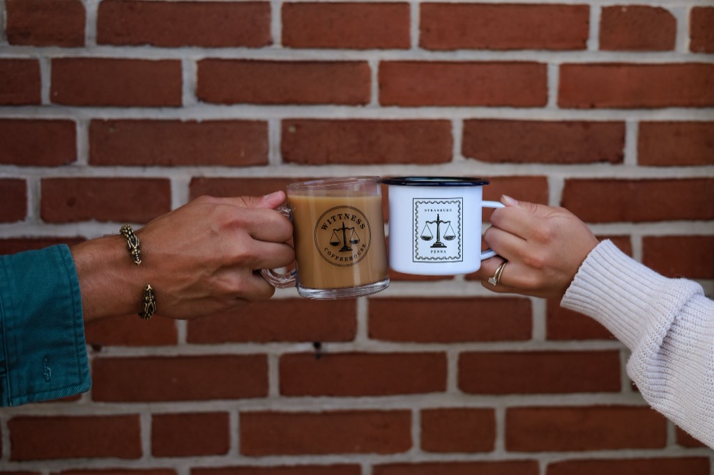 Two guests toasting with Wittness branded mugs in front of a brick wall